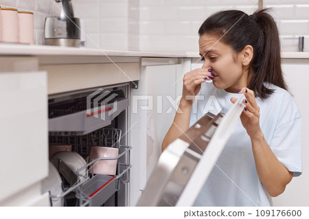 woman smells strange and terrible smell coming from dishwasher machine in kitchen woman smells strange and terrible smell coming from dishwasher machine in kitchen 109176600