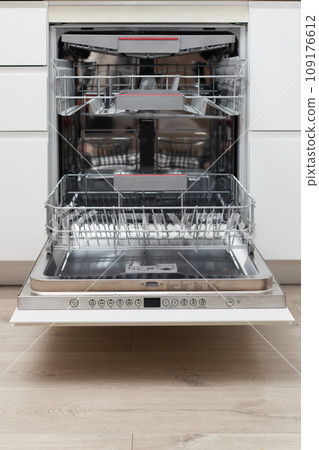 Modern built-in empty dishwasher with open door in the kitchen . 109176612