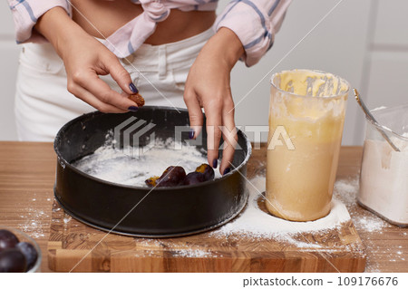 female hands cooking plum pie in light modern kitchen interior. female hands cooking plum pie in light modern kitchen interior. 109176676
