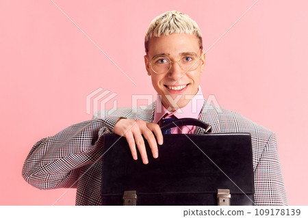 Sales manager. Young guy, employee smiling, wearing jacket holding briefcase against pink studio background 109178139
