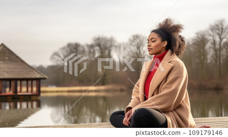 Tranquil woman meditates sitting in lotus pose on pier by calm river on autumn day Tranquil woman meditates sitting in lotus pose on pier by calm river on autumn day 109179146