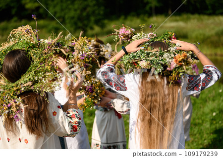 Girls in woven wreaths of different flowers and grass on a warm summer day. 109179239