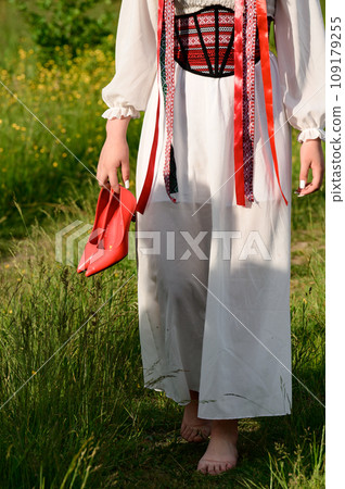 The girl, with her back turned and dressed in Ukrainian national clothes, walks barefoot in the field. 109179255