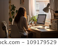 young woman working from home in front of a computer monitor. The apartment is minimalistic, with plants 109179529
