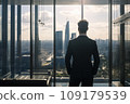 Young businessman standing in front of an office window, overlooking the city skyline 109179539