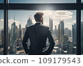 Young businessman standing in front of an office window, overlooking the city skyline 109179543