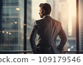 Young businessman standing in front of an office window, overlooking the city skyline 109179546