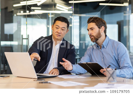 Business meeting, two business people serious concentrated discussing strategy and plans, sitting at table with documents inside office at workplace discussing communicating looking at laptop screen. 109179705