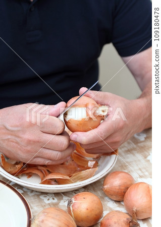 Man's hands peeling freh raw onion with kitchen knife on the kitchen table 109180478