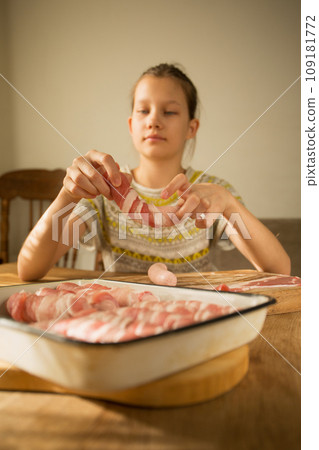 A girl prepares a traditional Christmas dish "Pigs in a blanket" Wraps sausages in bacon 109181772