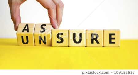 Assure or unsure symbol. Businessman turns wooden cubes and changes the concept word unsure to assure. Beautiful yellow table, white background, copy space. Business and assure or unsure concept. 109182635