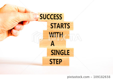 Success symbol. Concept words Success starts with a single step on wooden block. Beautiful white table white background. Businessman hand. Business success starts with single step concept Copy space Success symbol. Concept words Success starts with a single step on wooden block. Beautiful white table white background. Businessman hand. Business success starts with single step concept Copy space 109182638