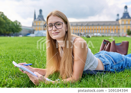 Young student girl lying on grass, educational building background 109184394