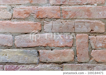 Ancient rough red brick wall with cracks and holes, close-up. Background texture 109184471