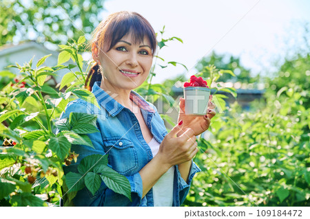 Happy woman in raspberry bushes garden, with cup ripe raspberries Happy woman in raspberry bushes garden, with cup ripe raspberries 109184472