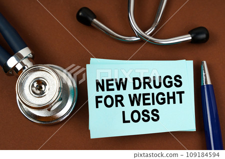 On a brown surface there is a stethoscope, a pen and blue stickers with the inscription - new drugs for weight loss On a brown surface there is a stethoscope, a pen and blue stickers with the inscription - new drugs for weight loss 109184594