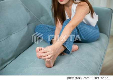 Asian beautiful female problems with foot at home, painful ankle injury, Young woman sitting on sofa holding her feet and stretch muscles have symptoms feeling pain, Health care and medical concept Asian beautiful female problems with foot at home, painful ankle injury, Young woman sitting on sofa holding her feet and stretch muscles have symptoms feeling pain, Health care and medical concept 109184860