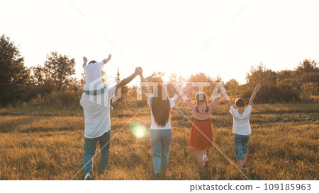 Strong friendly family with children walks raising hands across meadow at sunset 109185963