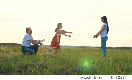 Little girl runs and embraces mother and father having fun in rural field 109185964