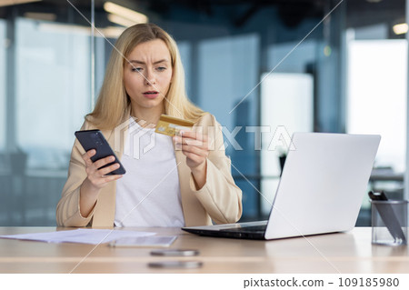 Frustrated sad upset woman working inside office, cheated business woman refused online money transfer, female worker displeased holding bank credit card and phone. 109185980