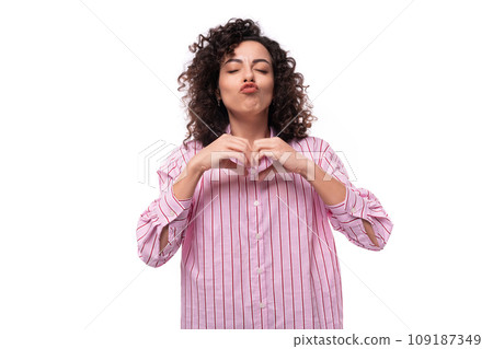 young authentic caucasian woman with curly black hair dressed in a pink shirt on a white background 109187349