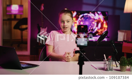 Happy child filming reaction video for gen Z viewers, preparing to look at online videos on laptop, handheld camera shot. Small girl recording reaction to internet clips for social media channels 109187384