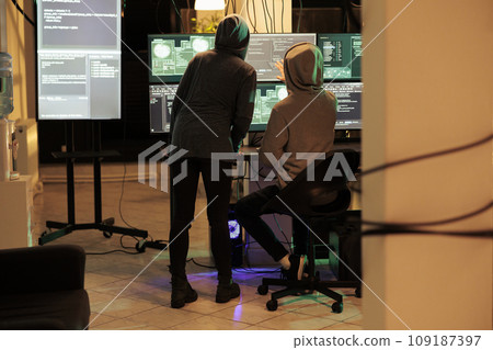 Team of cybercriminals cracking server encryption and hacking system, working on cyberterrorism at night. Young hackers doing criminal activity, stealing sensitive information. Team of cybercriminals cracking server encryption and hacking system, working on cyberterrorism at night. Young hackers doing criminal activity, stealing sensitive information. 109187397