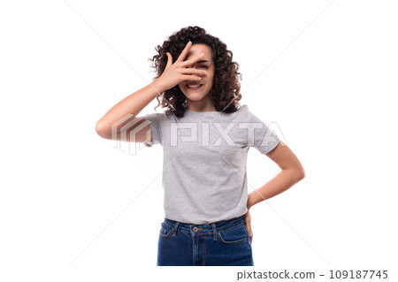 young european woman with black curly hair in a gray basic t-shirt looks happy on a white background 109187745