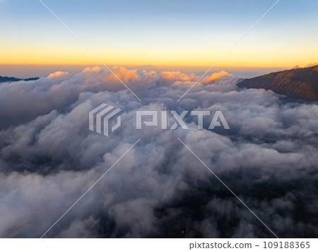 Aerial view of flowing fog waves on mountain tropical rainforest,Bird eye view image over the clouds Amazing nature background with clouds and mountain peaks in indonesia 109188365