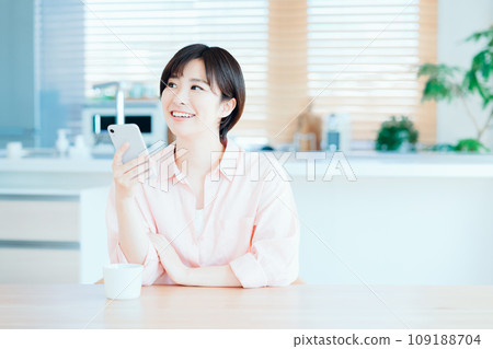 A woman relaxing while using a smartphone in the living room. A woman relaxing while using a smartphone in the living room. 109188704