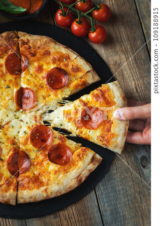 A slice of hot Italian pizza with stretching cheese. Pizza pepperoni on a dark wooden background A slice of hot Italian pizza with stretching cheese. Pizza pepperoni on a dark wooden background 109188915