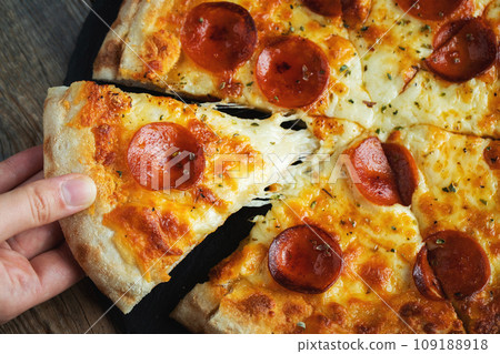 A slice of hot Italian pizza with stretching cheese. Pizza pepperoni on a dark wooden background 109188918