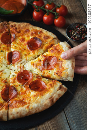 A slice of hot Italian pizza with stretching cheese. Pizza pepperoni on a dark wooden background A slice of hot Italian pizza with stretching cheese. Pizza pepperoni on a dark wooden background 109188927