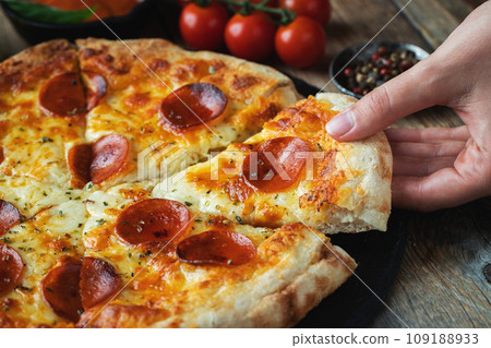 A slice of hot Italian pizza with stretching cheese. Pizza pepperoni on a dark wooden background 109188933