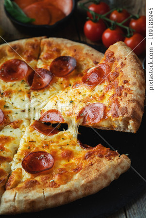 A slice of hot Italian pizza with stretching cheese. Pizza pepperoni on a dark wooden background 109188945
