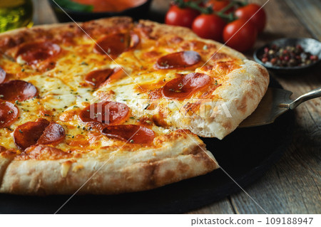 A slice of hot Italian pizza with stretching cheese. Pizza pepperoni on a dark wooden background A slice of hot Italian pizza with stretching cheese. Pizza pepperoni on a dark wooden background 109188947