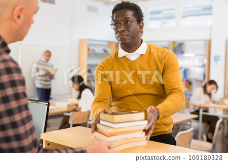 Young adult man returning books at library Young adult man returning books at library 109189328