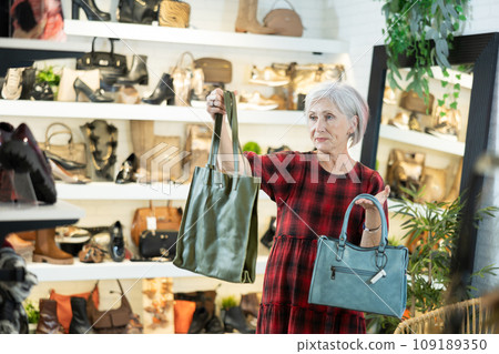 Elderly woman chooses handbag in store 109189350