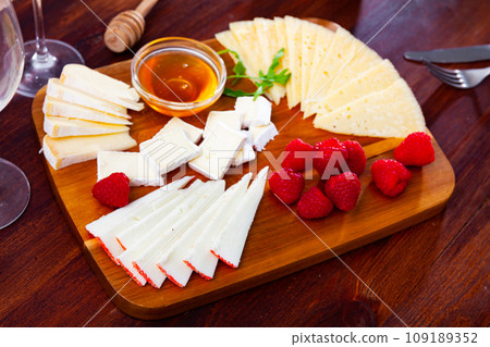 Cheese platter on wooden board with raspberries and honey 109189352