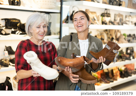Young and elderly women choosing boots in store Young and elderly women choosing boots in store 109189379
