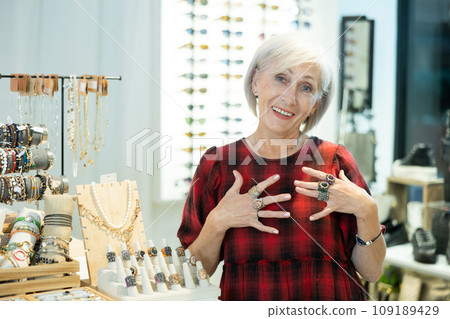 Elderly woman client enthusiastically examines showcase counter with jewelry 109189429