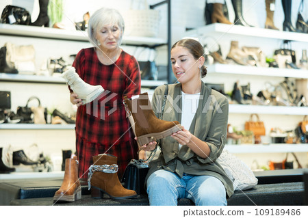 Young girl with elderly mother choosing demi-season footwear in shoe boutique Young girl with elderly mother choosing demi-season footwear in shoe boutique 109189486