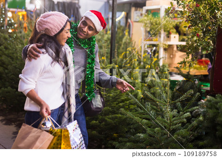 Family couple choosing christmas tree at christmas fair Family couple choosing christmas tree at christmas fair 109189758