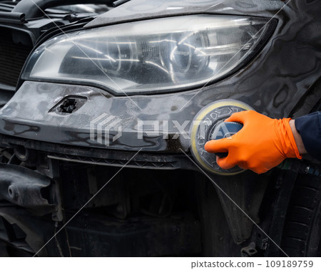 A mechanic sands the putty on a car body with a machine. Repair after an accident. A mechanic sands the putty on a car body with a machine. Repair after an accident. 109189759