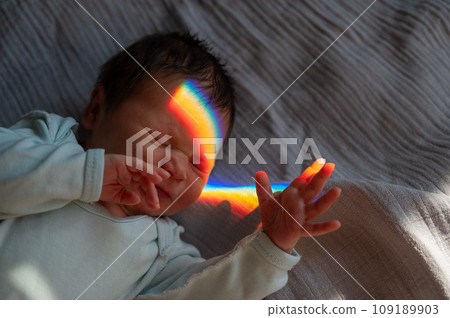 Close-up portrait of a newborn boy with a prism beam on his face. Rainbow. 109189903