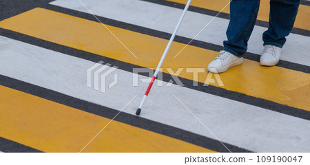 Close-up of the legs of a blind woman crossing the road at a crosswalk with a cane.  109190047
