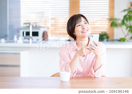 A woman uses a smartphone while drinking coffee in the living room. 109190146