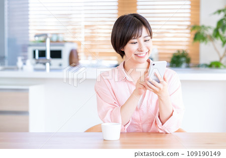 一位女士在客廳喝咖啡時使用智慧型手機。 109190149