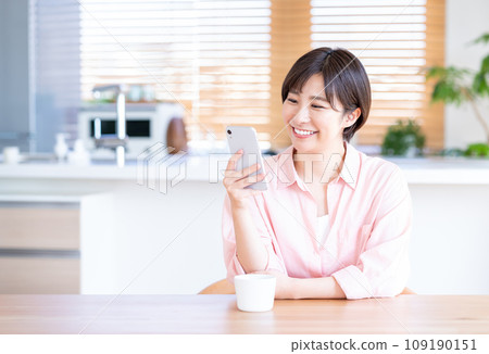 一位女士在客廳喝咖啡時使用智慧型手機。 109190151