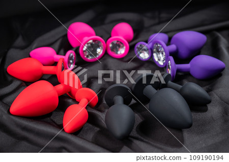 A set of silicone anal plugs in different colors and sizes on a black silk sheet.  109190194